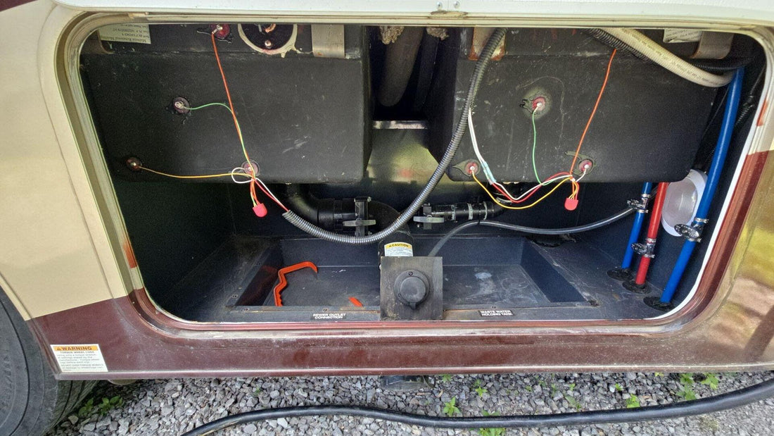 Open RV wet bay showing black and grey holding tanks and dump valves